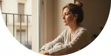 Mujer sentada junto a una ventana con gesto pensativo, reflejando ansiedad anticipatoria asociada a la agorafobia