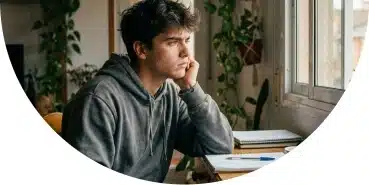 Joven sentado en su escritorio mirando por la ventana, mostrando ansiedad y bloqueo emocional